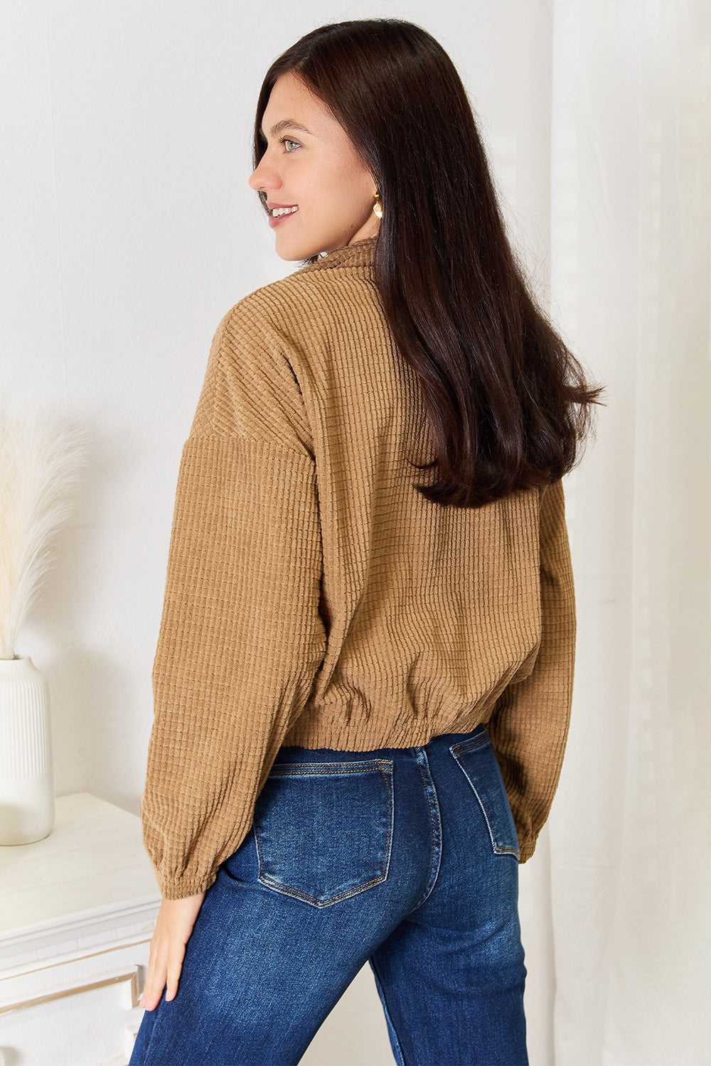 Woman wearing a brown ribbed Long Sleeve Dropped Shoulder Jacket and blue jeans against a white wall.