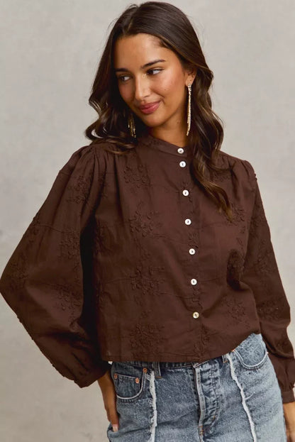 Woman wearing a brown embroidered button-up blouse with balloon sleeves and high-waisted jeans.