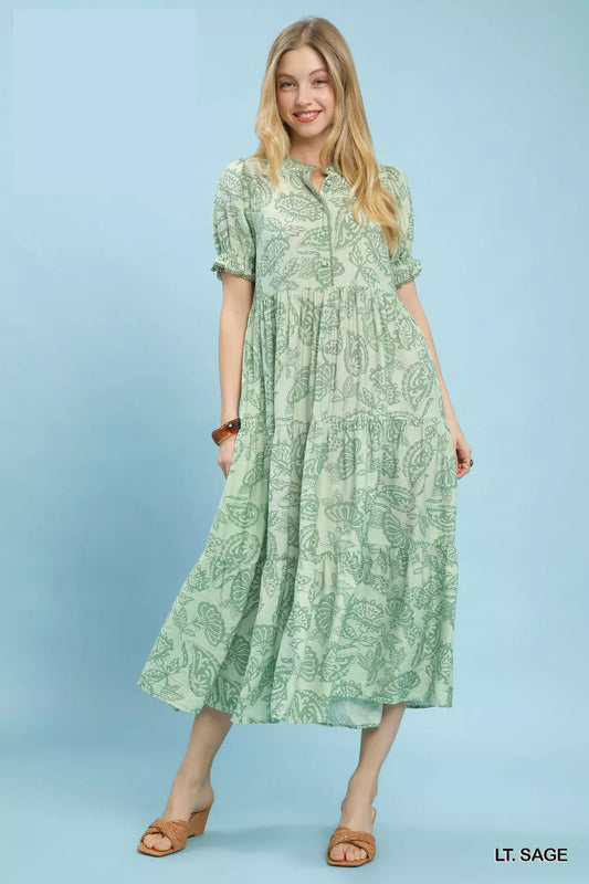 Woman wearing an Umgee Paisley Print Tiered Midi Dress on a blue background and brown slip on heeled sandals