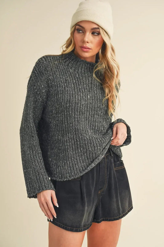 Woman in a gray ribbed knit sweater, black denim shorts, and cream beanie hat