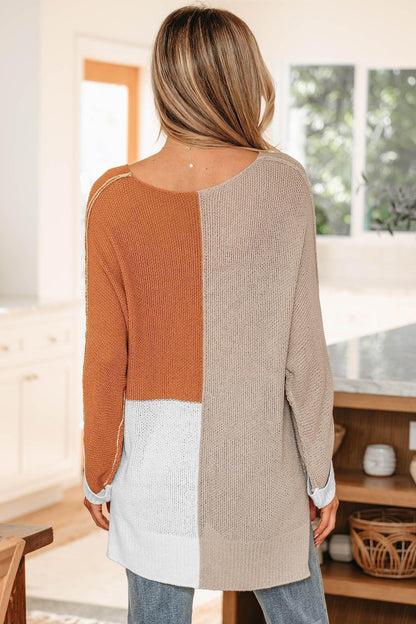 Woman wearing a colorblock knit sweater in beige, rust, and white, standing in a modern kitchen