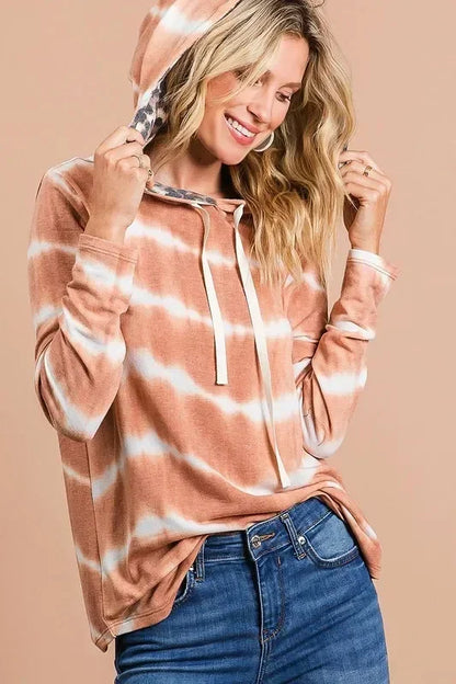 Woman wearing a brown and white tie-dye hooded sweatshirt with drawstrings and blue jeans