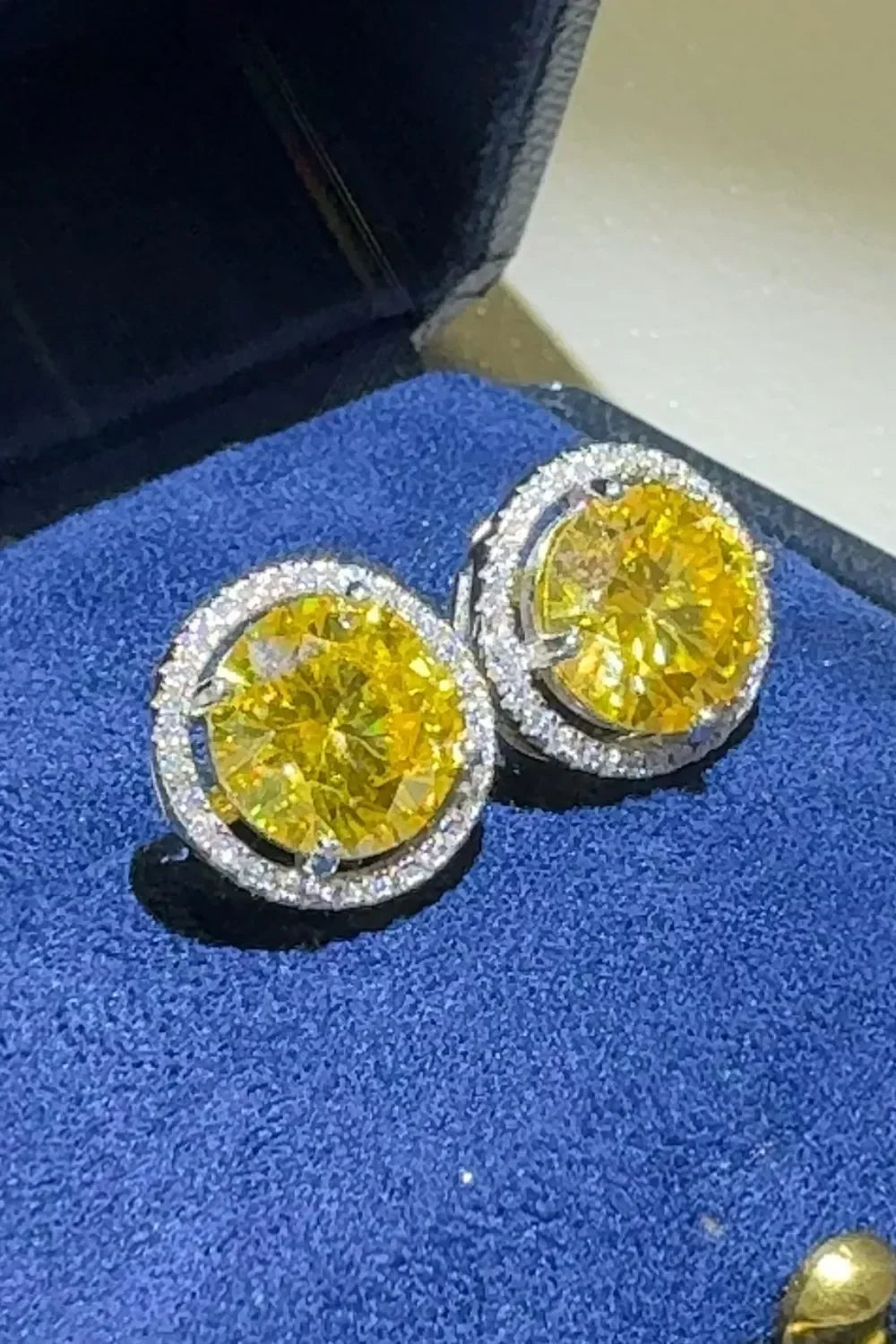 Yellow gemstone stud earrings with diamond halos in a blue velvet jewelry box.
