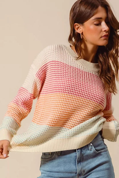 Woman in a pastel striped knit sweater and light blue jeans, neutral background