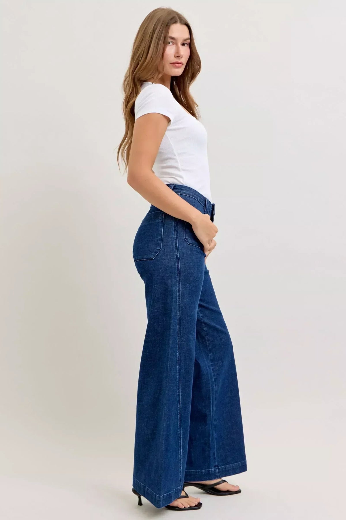 Woman in white fitted t-shirt and high-waisted wide-leg blue jeans, side view