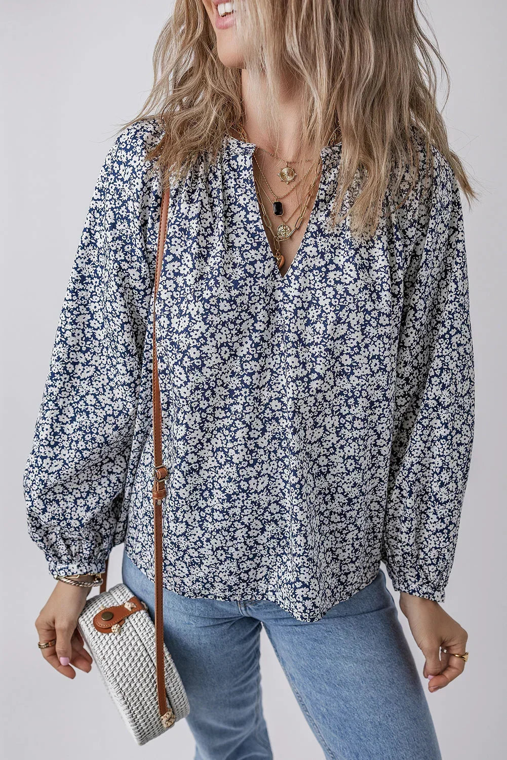 Woman wearing a blue floral blouse with balloon sleeves, light jeans, and woven crossbody bag