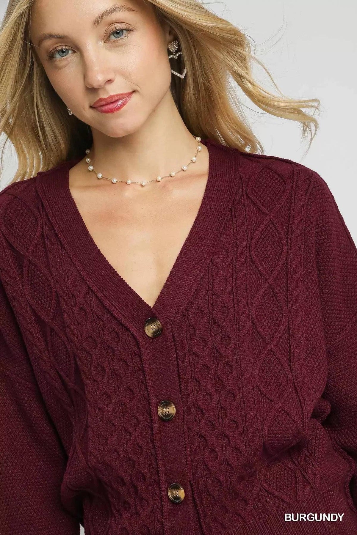 Woman wearing a burgundy cable-knit button-front cardigan with V-neck detail.