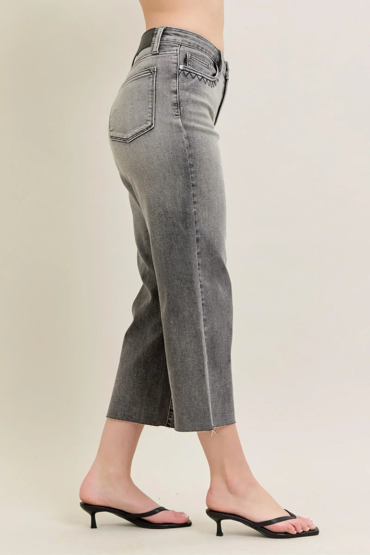 Woman wearing high-rise, cropped grey jeans with raw hem and black heeled sandals