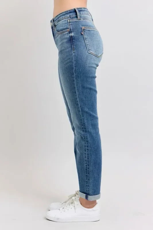 Side view of woman wearing mid-rise blue denim jeans with rolled cuffs and white sneakers