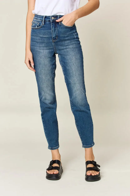Woman wearing high-waisted blue jeans and black sandals on a neutral background