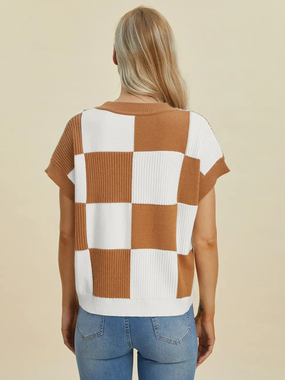 Woman wearing a brown and white checkered short sleeve knit top with blue jeans, back view.