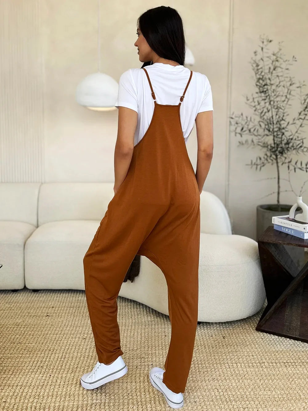 Woman in rust brown relaxed overalls and white t-shirt, casual indoor setting