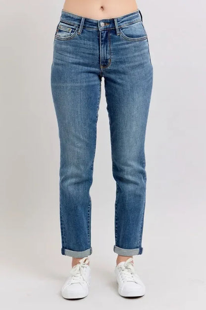 Woman wearing relaxed-fit blue jeans with rolled cuffs and white sneakers on a plain background.