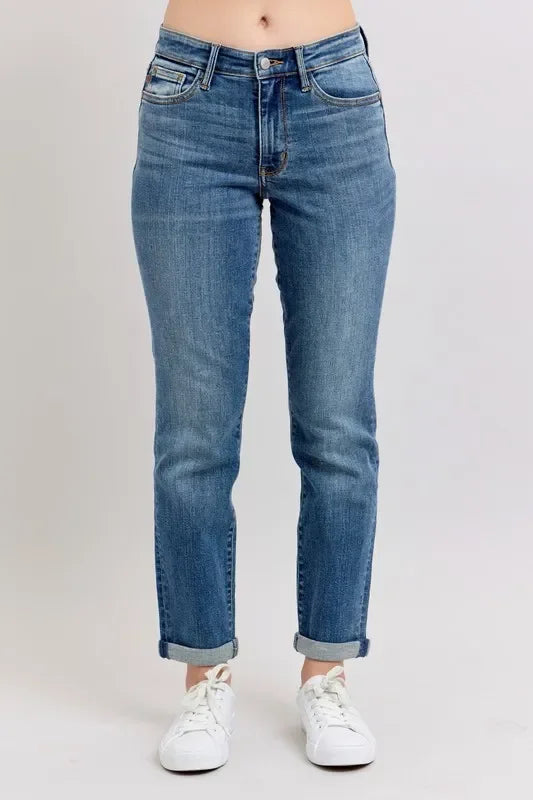 Woman wearing relaxed-fit blue jeans with rolled cuffs and white sneakers on a plain background.