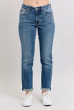 Woman wearing relaxed-fit blue jeans with rolled cuffs and white sneakers on a plain background.