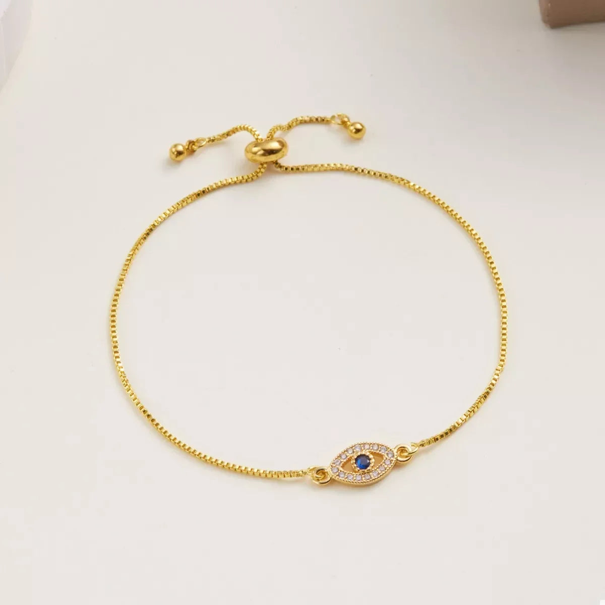 Gold adjustable bracelet with evil eye charm and blue center stone on neutral background
