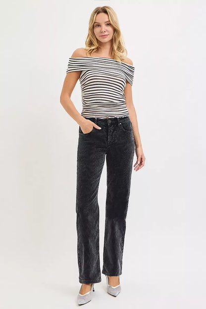 Woman in off-the-shoulder striped top and black high-waisted jeans standing against white background