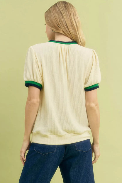 Back view of woman in ecru short sleeve knit top with green trim and dark denim jeans