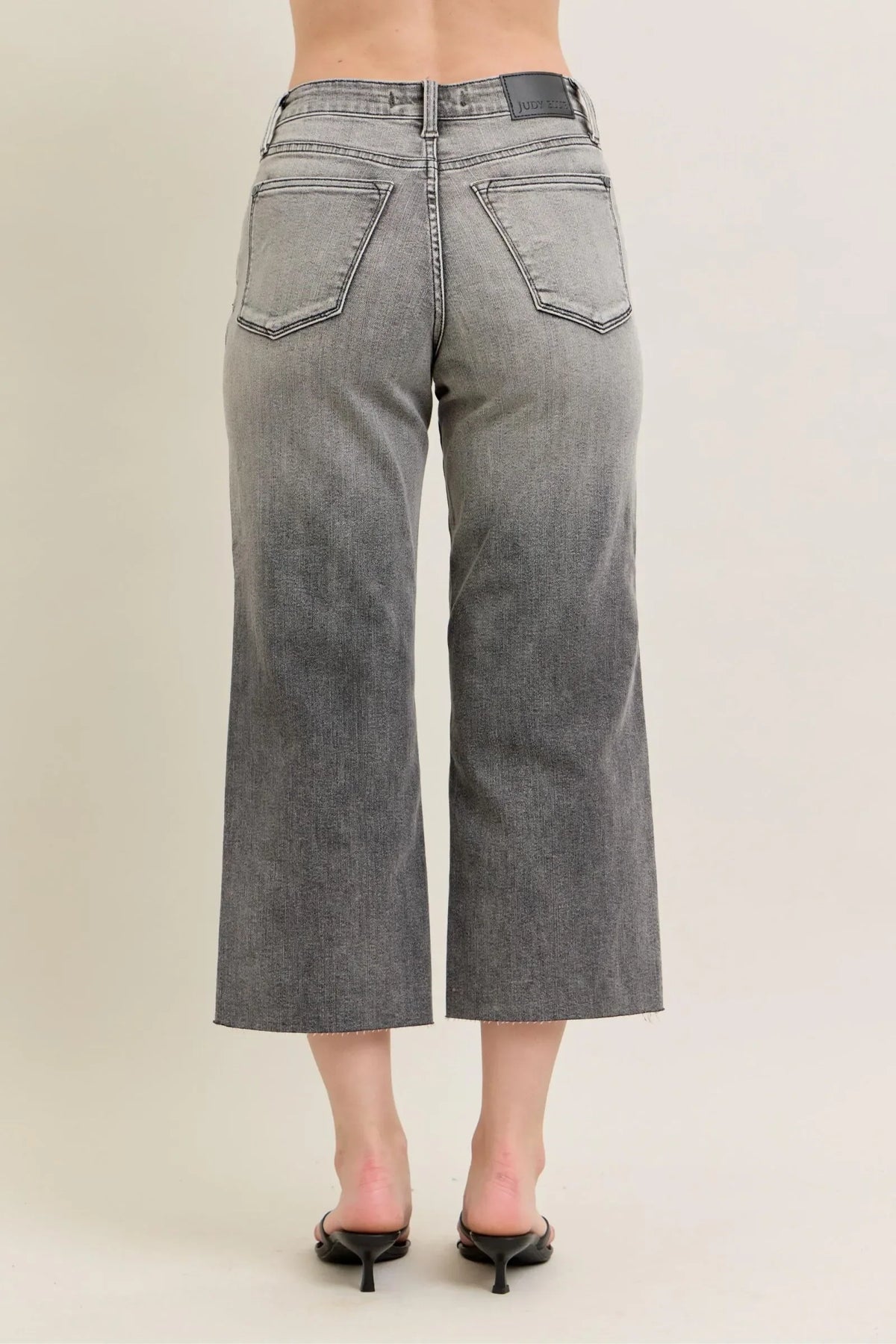 Back view of woman wearing high-waisted grey wide-leg cropped jeans and black heels