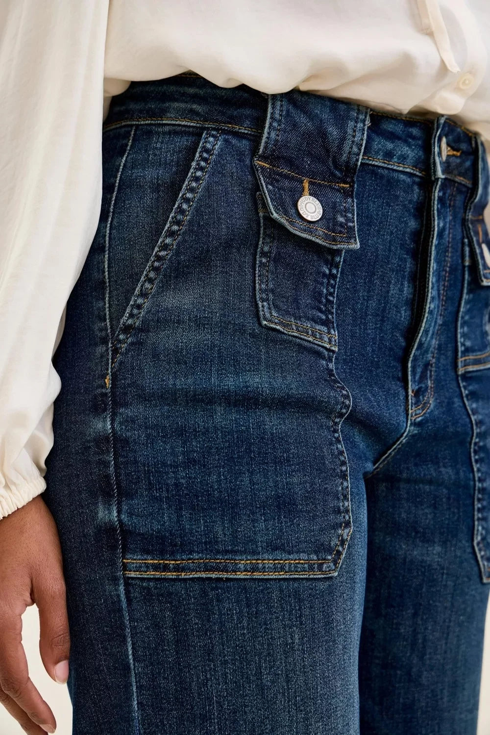 Close-up of high-waisted dark wash denim jeans with large front pockets and button details