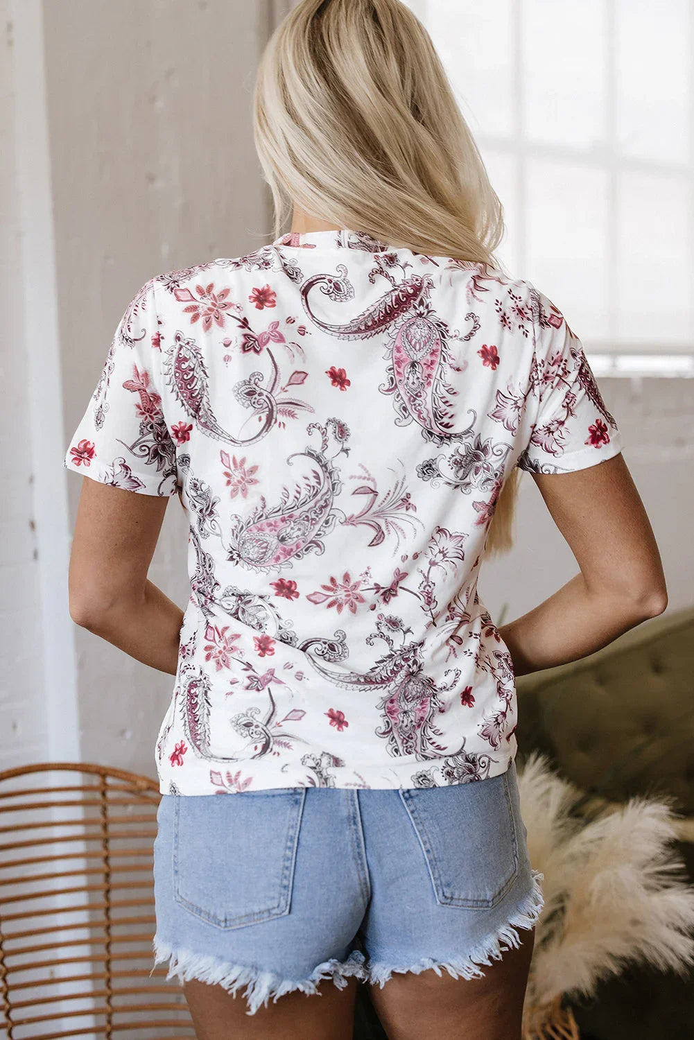 Woman in paisley print white t-shirt and frayed denim shorts standing indoors