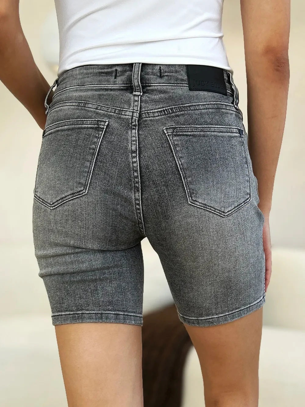 Back view of high-waisted grey denim shorts with pockets, worn with a white top