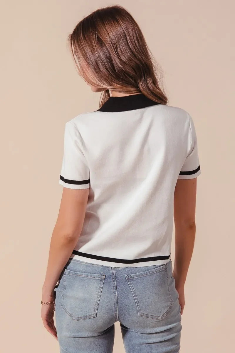 Woman wearing white short-sleeve knit top with black trim and light-wash jeans, back view