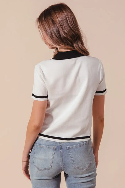 Woman wearing white short-sleeve knit top with black trim and light-wash jeans, back view