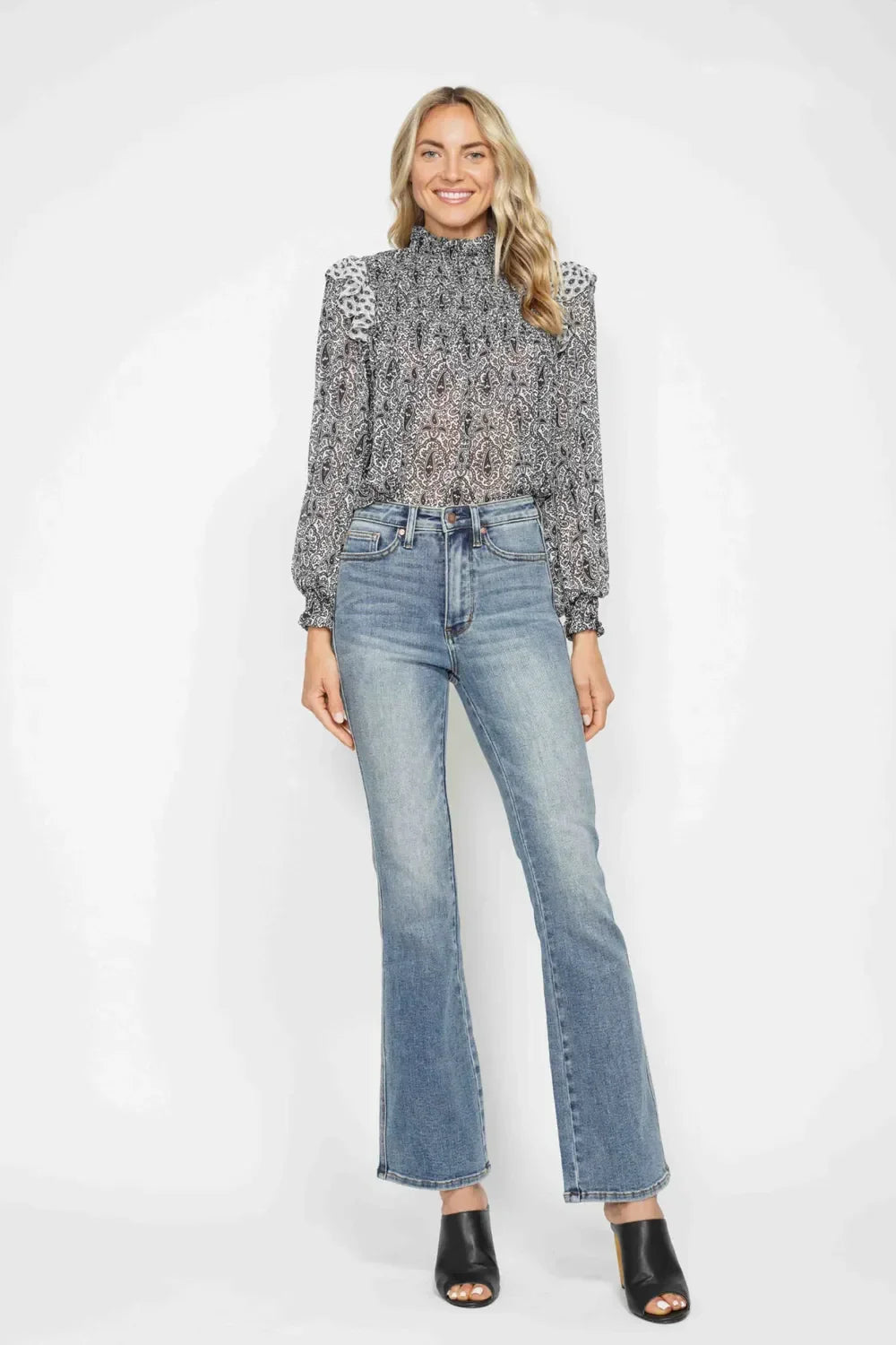 Woman wearing a black and white patterned blouse with high-waisted blue jeans and black mules