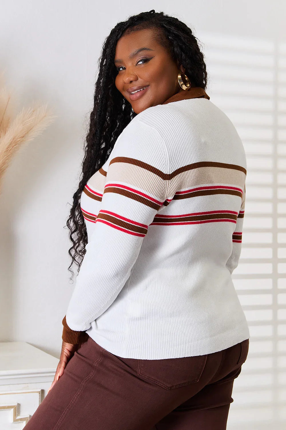 Woman wearing a white ribbed sweater with red and brown stripes and brown pants