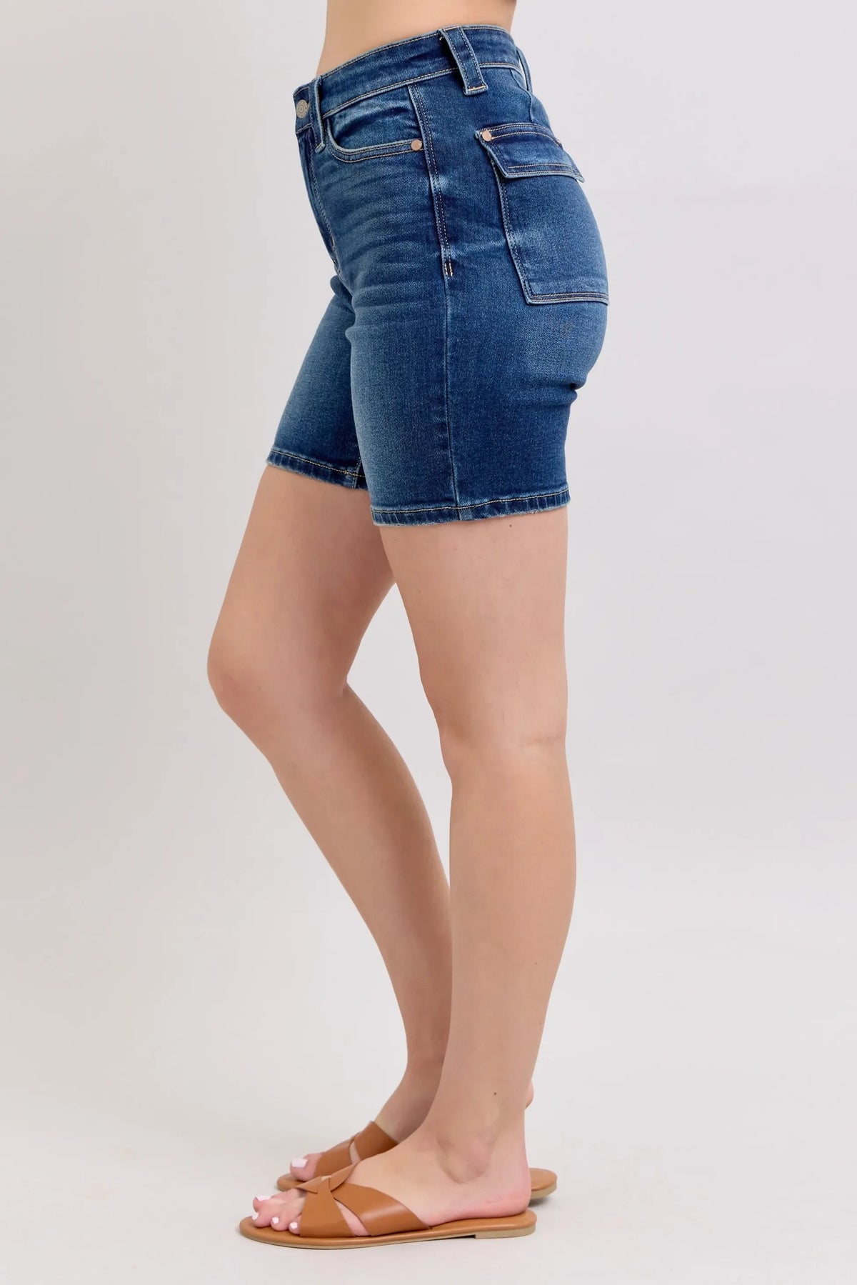 Woman wearing high-waisted denim Bermuda shorts and tan slip-on sandals