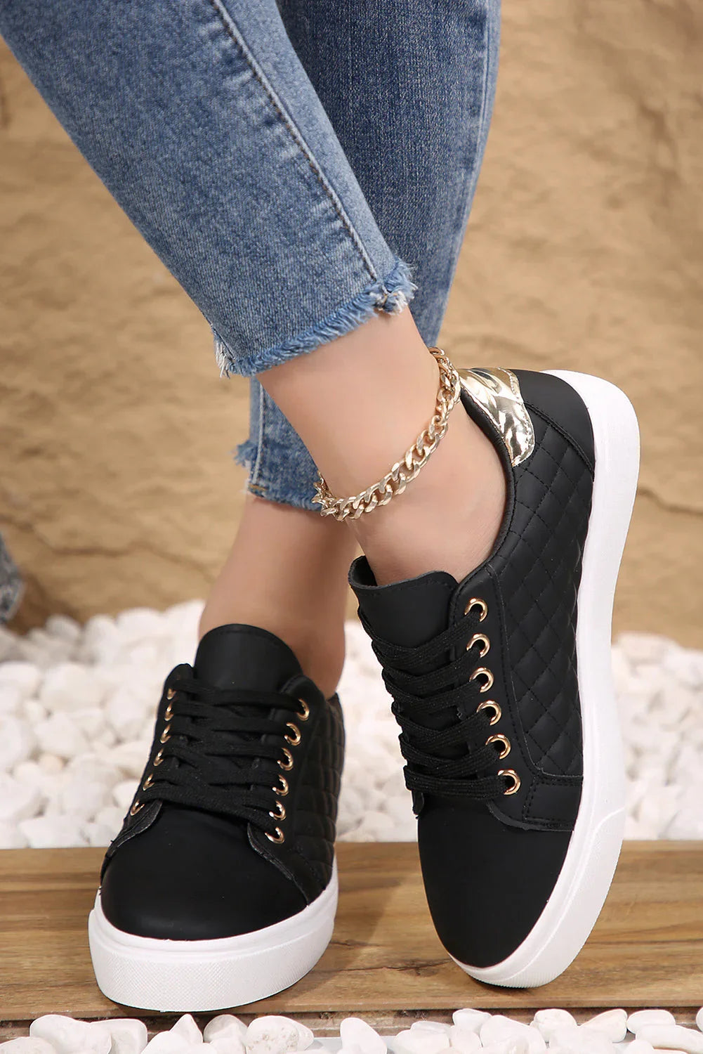 Woman wearing black quilted sneakers with white soles and gold accents, paired with frayed hem jeans