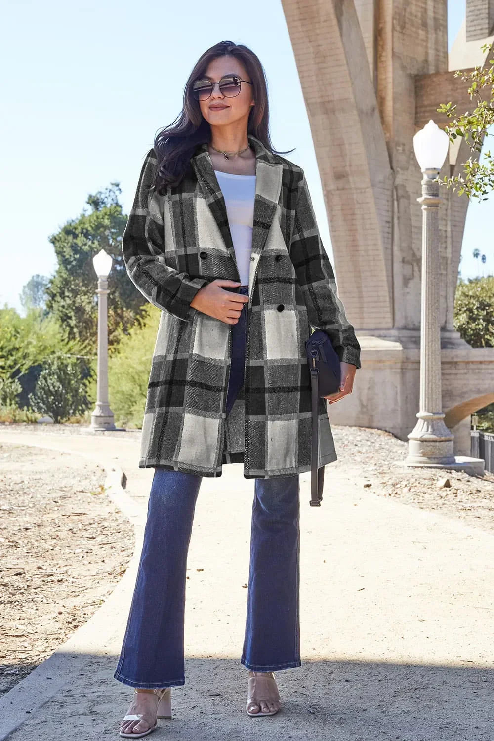 Woman wearing black and white plaid coat, white top, and flared jeans outdoors