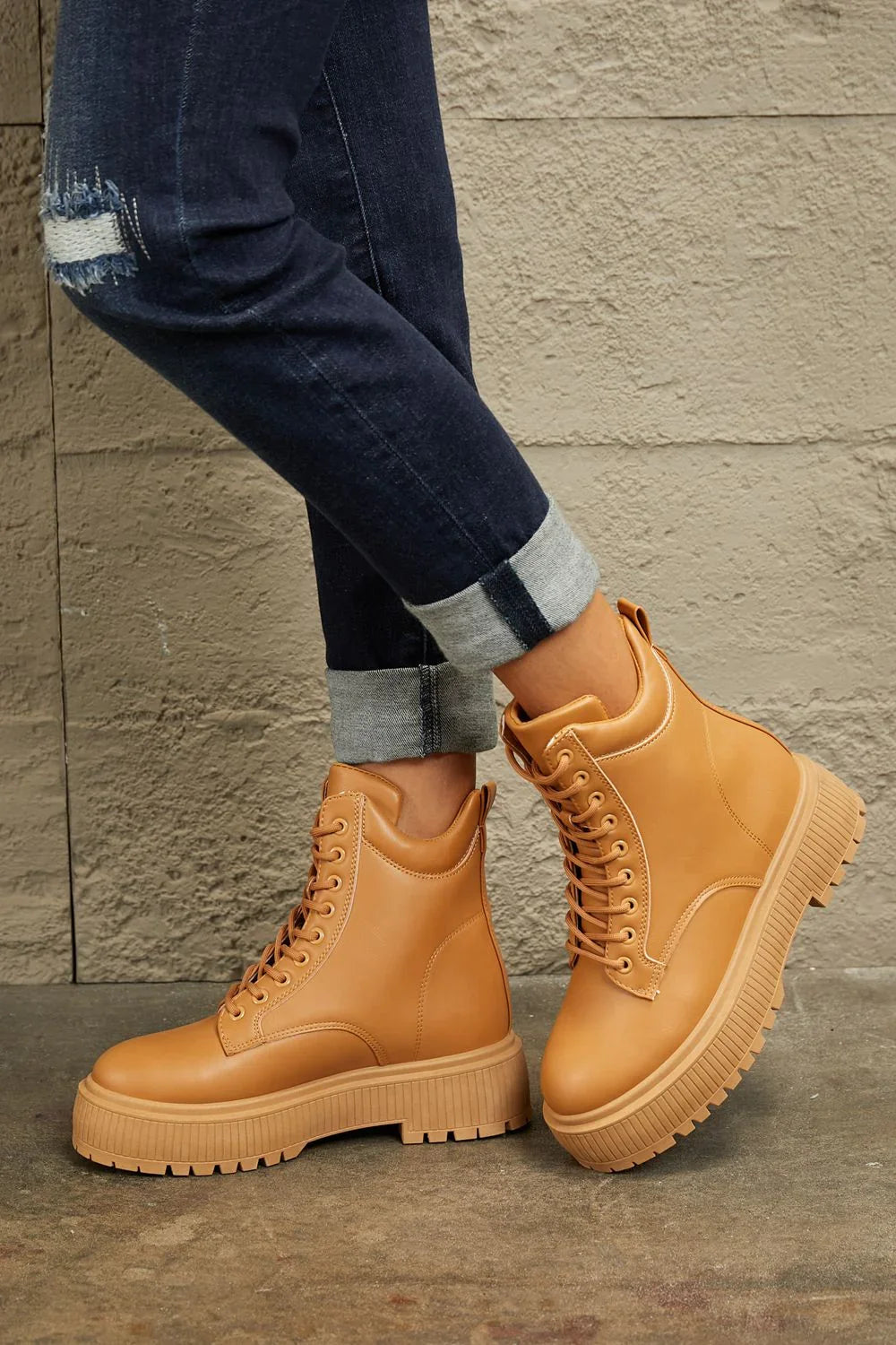Tan lace-up platform boots styled with cuffed dark jeans on concrete background
