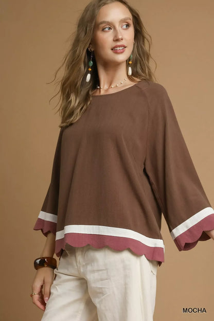 Woman wearing loose mocha top with scalloped hem, white stripe and wide sleeves