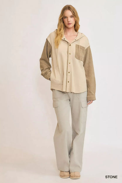Woman wearing a beige hooded button-up jacket with textured sleeves and light cargo pants