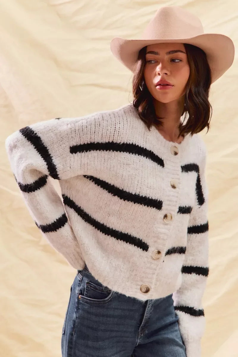 Woman wearing a beige hat, white knit cardigan with black stripes, and blue jeans