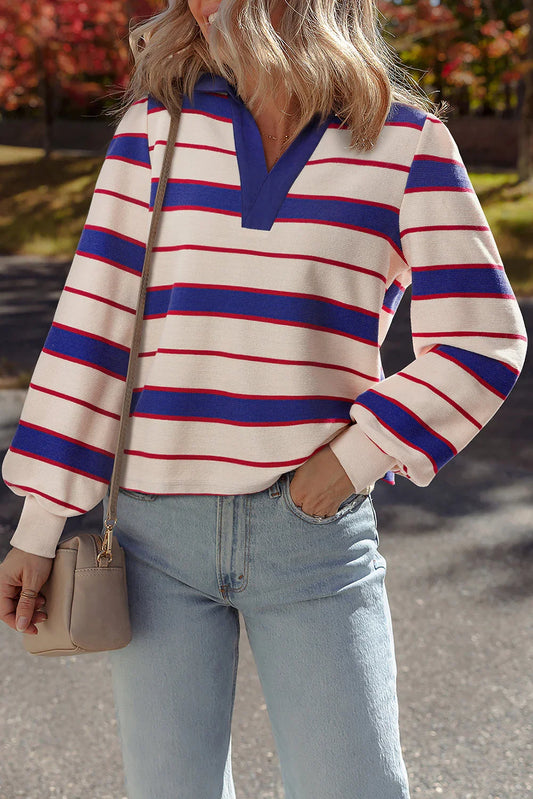 Woman wearing a cream top with blue and red stripes, light wash jeans, and a beige purse outdoors.