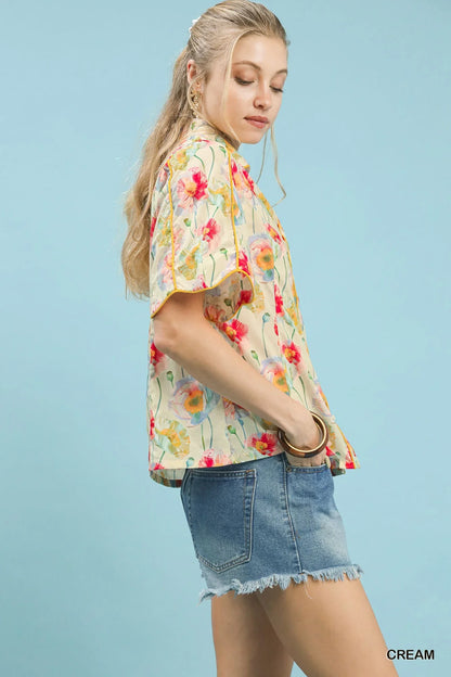 Woman wearing short sleeve cream floral blouse and denim fringe shorts against blue background