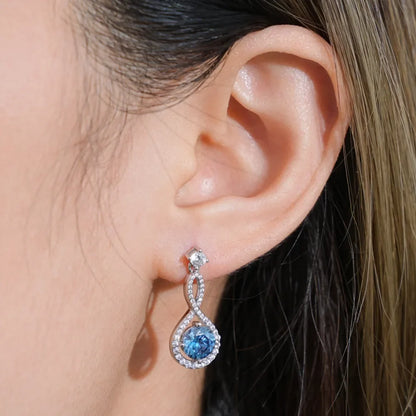 Close-up of a woman's ear wearing a silver drop earring with a blue gemstone and pavé accents