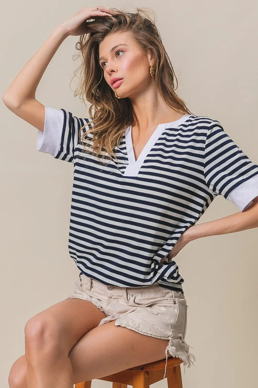 Woman wearing a BiBi Contrast Striped Notched Knit Top with white trim and beige distressed shorts, seated on a stool.