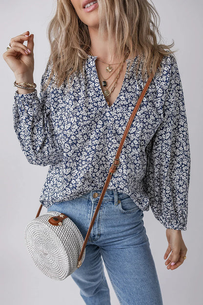 Woman wearing a blue floral blouse, light wash jeans, layered necklaces, and a round woven crossbody bag.