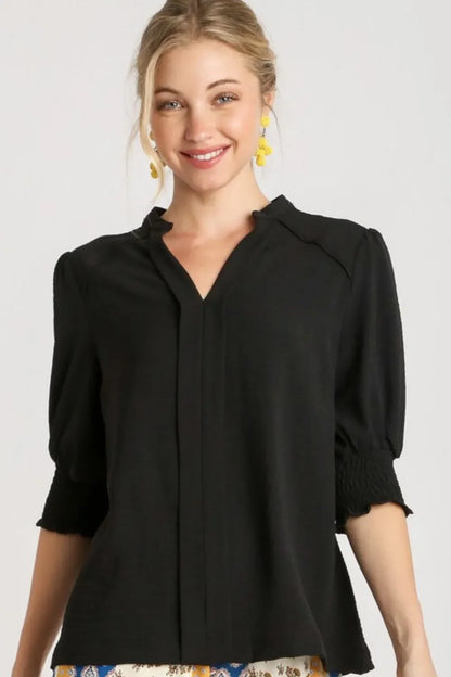 Woman wearing black V-neck blouse with puff sleeves and smocked cuffs