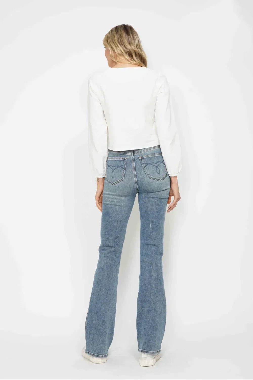 Woman in a white long sleeve blouse and high-waisted blue flared jeans, back view