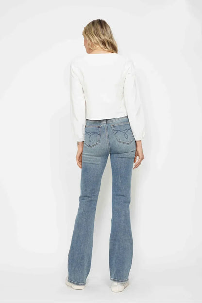 Woman in a white long sleeve blouse and high-waisted blue flared jeans, back view