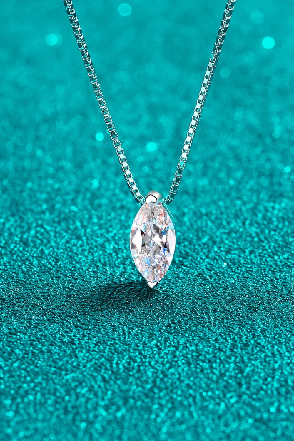 Marquise-cut diamond pendant necklace on a silver chain displayed against turquoise glitter.