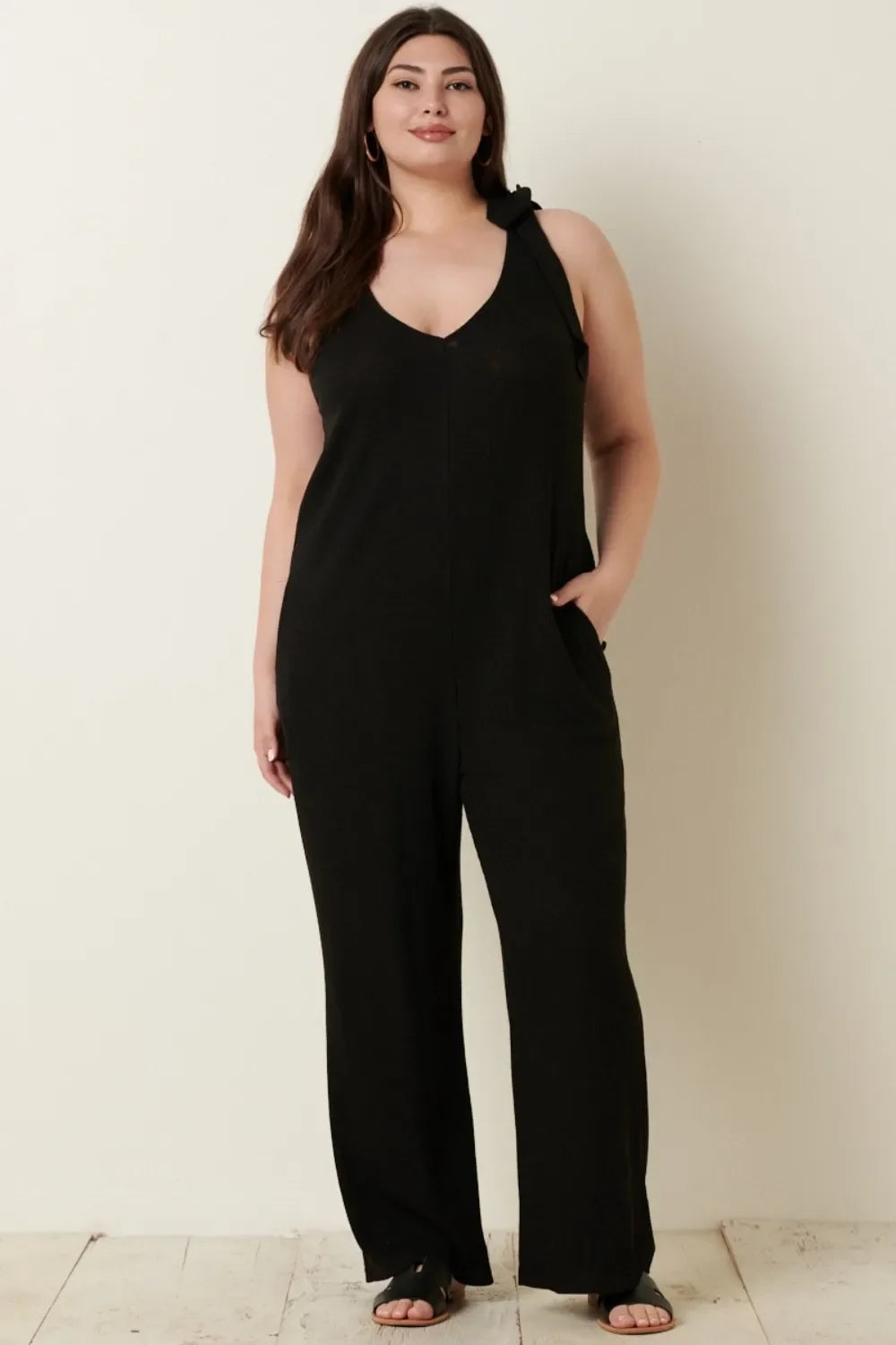 Woman modeling a black sleeveless wide-leg jumpsuit with a v-neck and tie shoulder detail.
