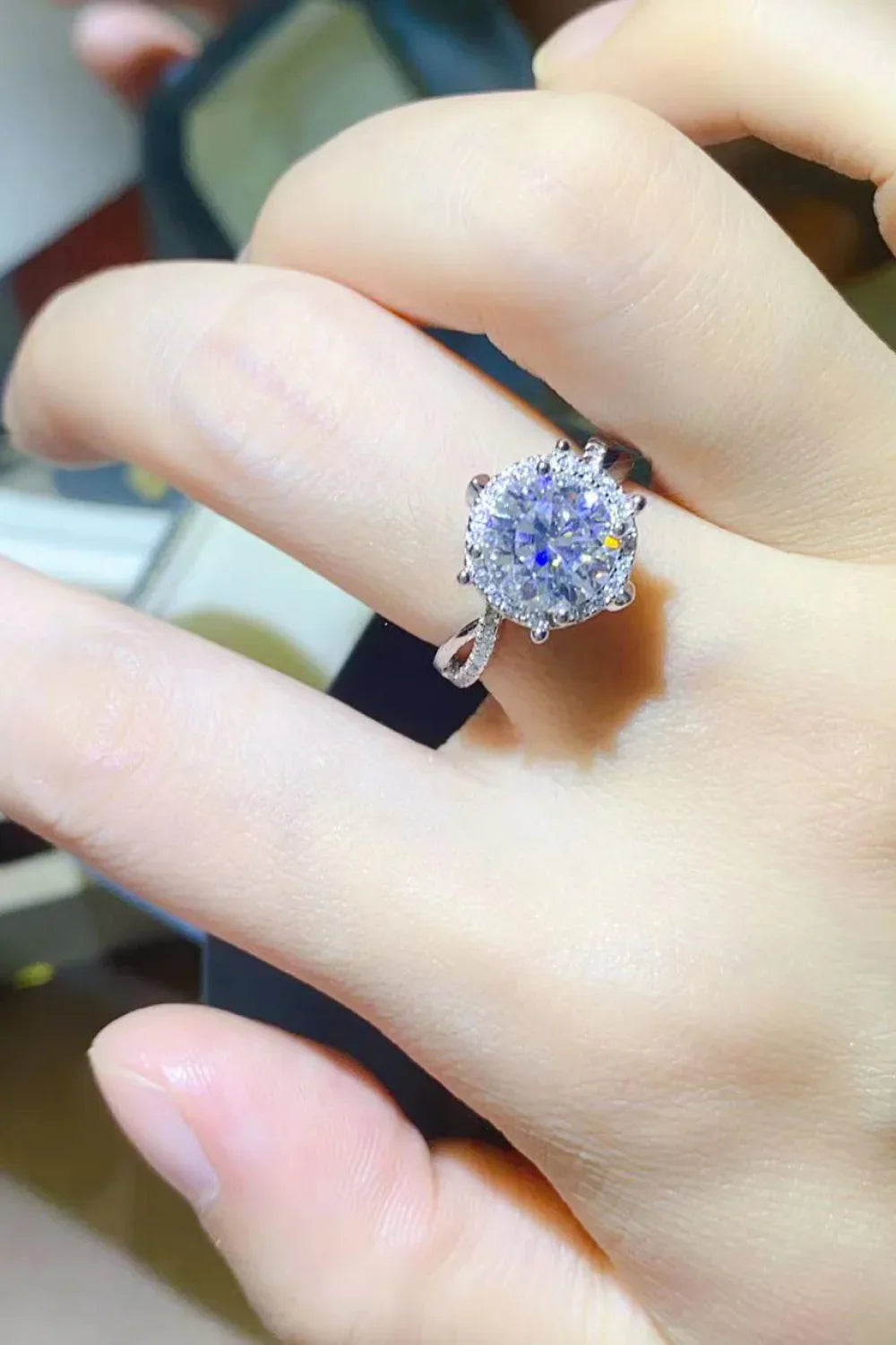 Hand wearing a silver ring with a large round-cut gemstone and halo setting