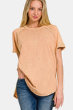 Woman wearing a peach-toned short sleeve relaxed t-shirt and blue jeans on white background