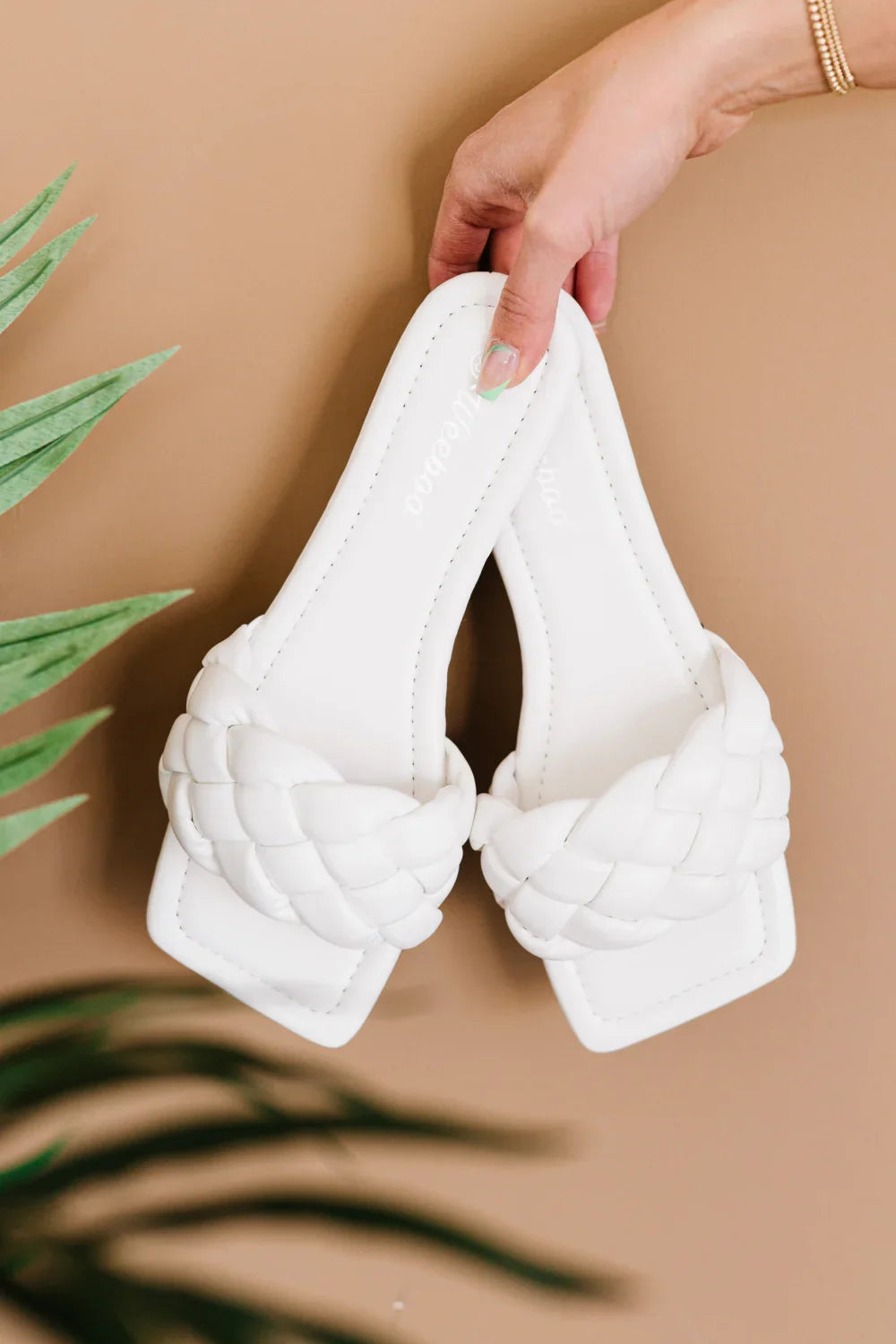 Hand holding white braided slide sandals with square toes against neutral background